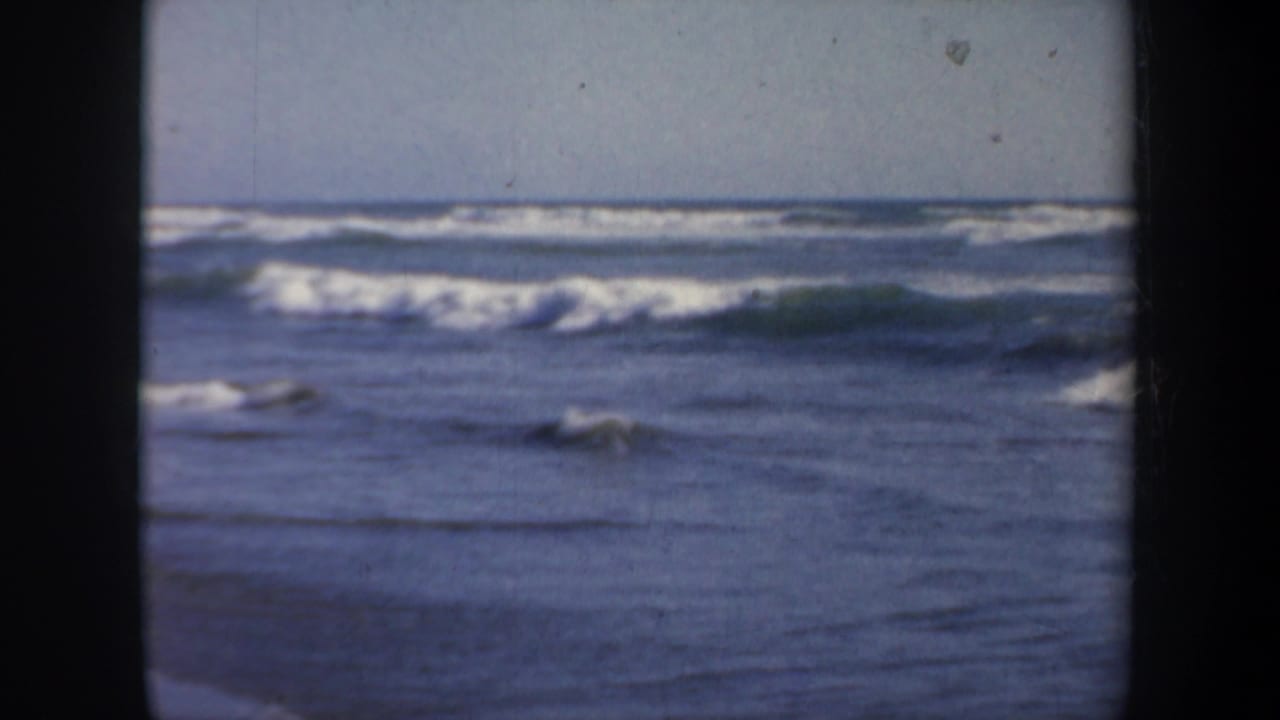 Low waves break across the frame with a pale horizon and dark 8mm side borders.