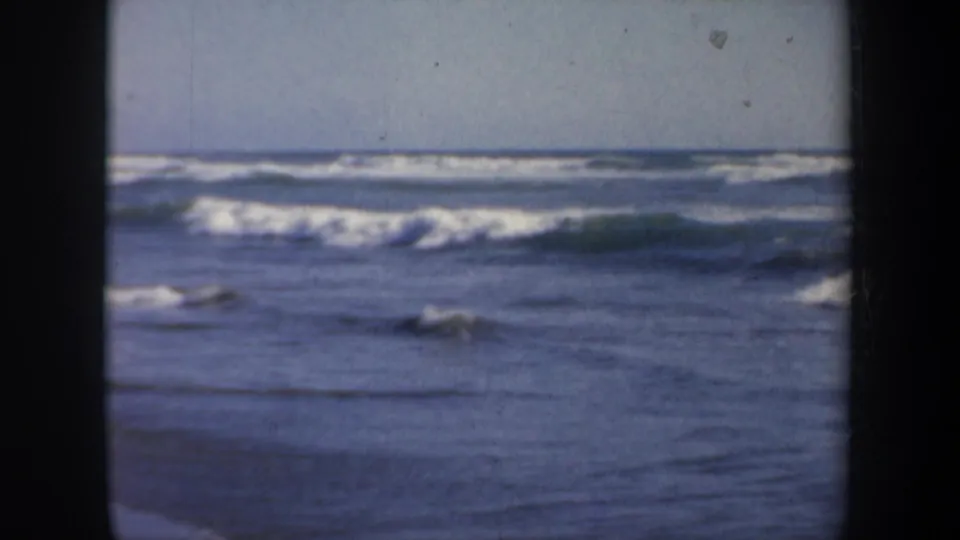 1957 San Francisco shoreline view with layered ocean waves, whitecaps, muted blue water, and visible 8mm film borders.