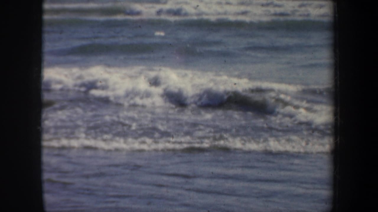 Ocean surf breaks under a distant horizon with dark film borders.