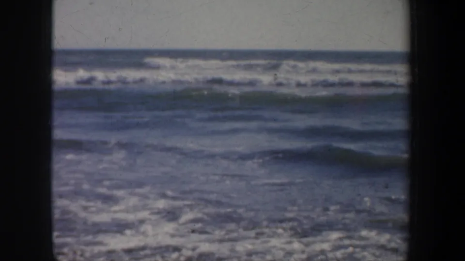 The frame shows a choppy Pacific surf view from the 1957 San Francisco home movie, with wave bands and dark film edges.