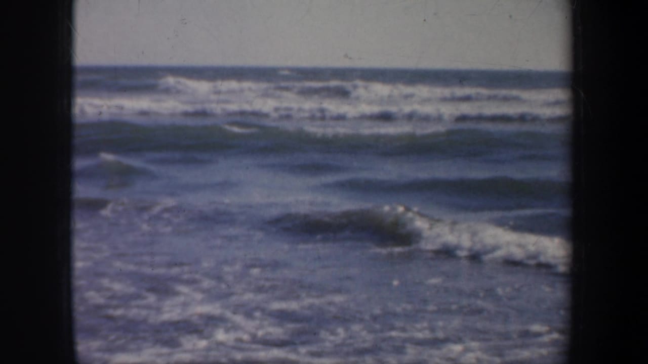 Ocean waves viewed past a dark pier edge and railing.