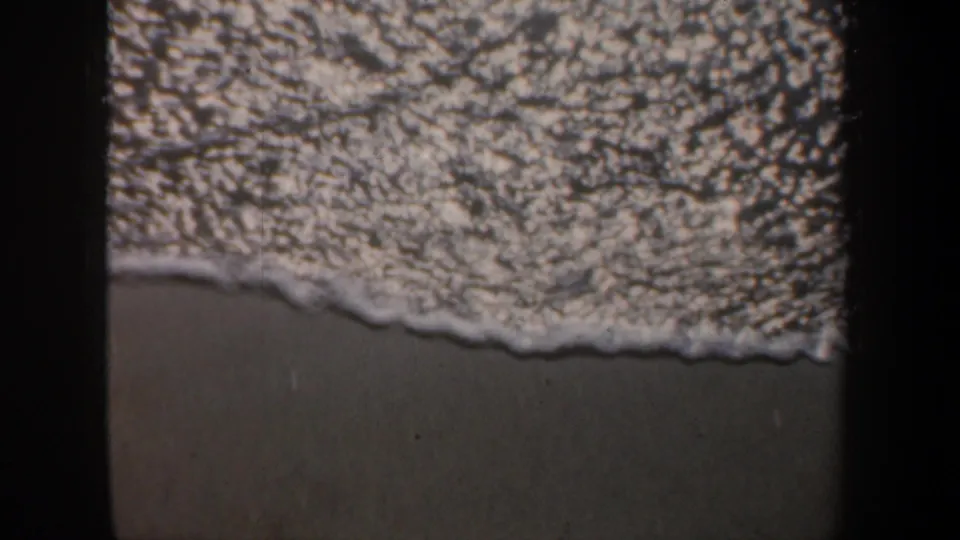 1957 San Francisco 8mm frame with a curved foam edge crossing wet sand, bordered by dark 8mm frame shadows.