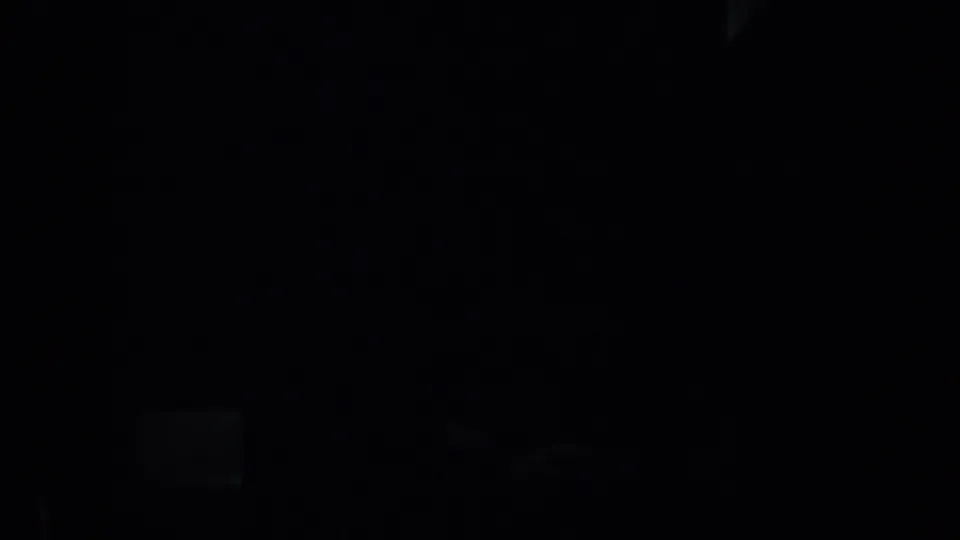 A dark underexposed 1957 San Francisco 8mm frame with a faint bright patch near the lower left and indistinct shadow forms.