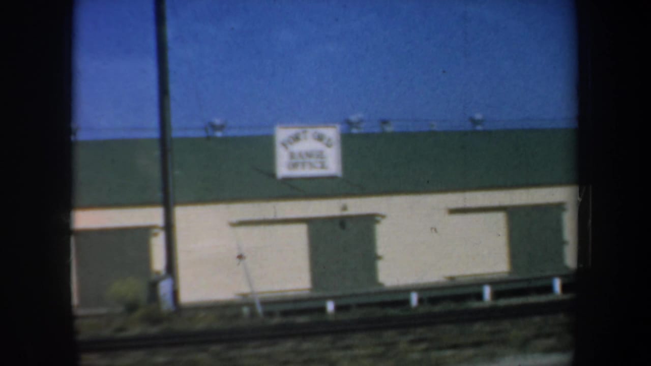 Roadside building with a Fort Ord Range Office sign seen through dark train-window framing.