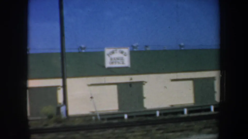 1957 8mm frame showing a Fort Ord Range Office building from a moving train or vehicle, with dark window edges in the foreground.