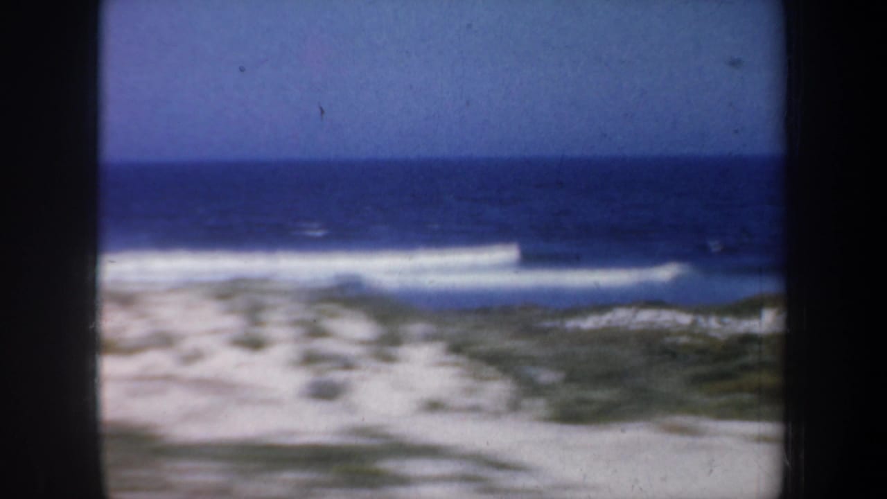 White surf line rolls toward a sandy beach with dunes in the foreground.