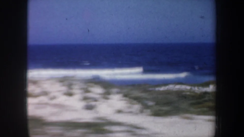 Passing 1957 San Francisco coastal view with white surf, blue water, tan sand, and dune vegetation.