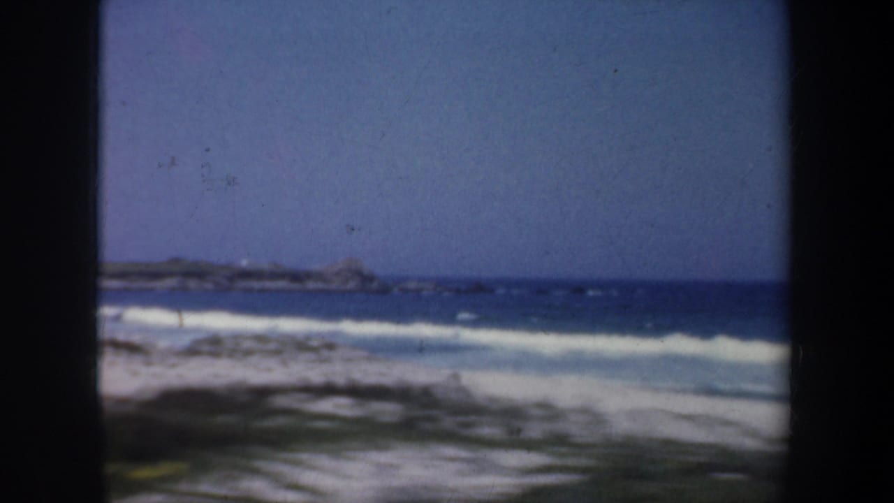 Surf, beach, and distant shoreline framed by dark vertical film edges.
