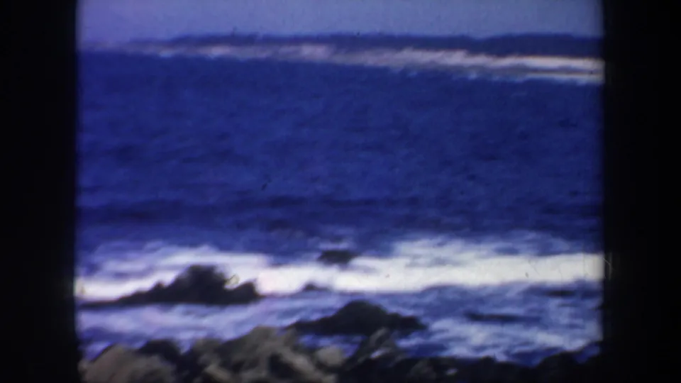 1957 San Francisco-area coastal shot with white surf breaking over rocks and blue water framed by dark 8mm borders.