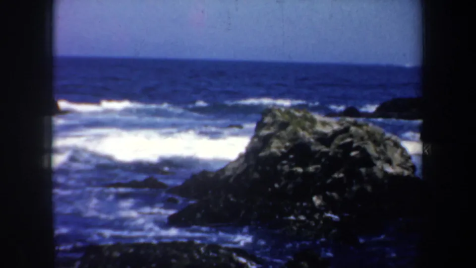 1957 8mm coastal frame showing Pacific surf breaking around offshore rock formations near San Francisco, California.