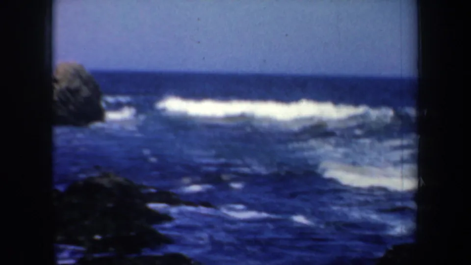 1957 8mm coastal frame with open blue water, white wave crests, and dark shoreline rocks near San Francisco, California.