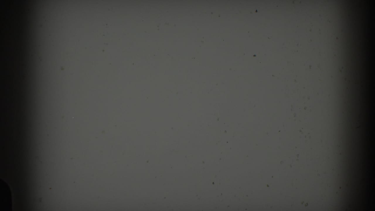 Dark opening frame from 1959 8mm Barcelona footage, showing mostly blank film surface with grain, dust, and gate shadow.