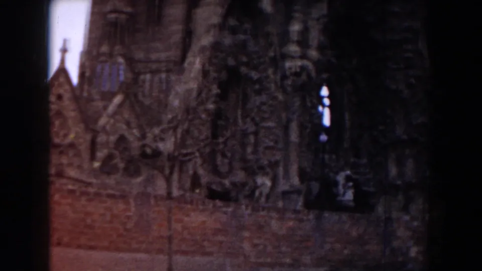 Dark 1959 Barcelona 8mm view of a Gothic religious building with stone towers, pointed details, and a brick wall in front.