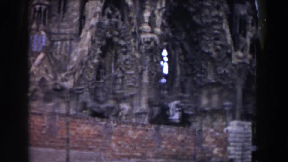 1959 Barcelona home-movie frame showing carved church stonework, arched details, brick foreground wall, and dark film edges.