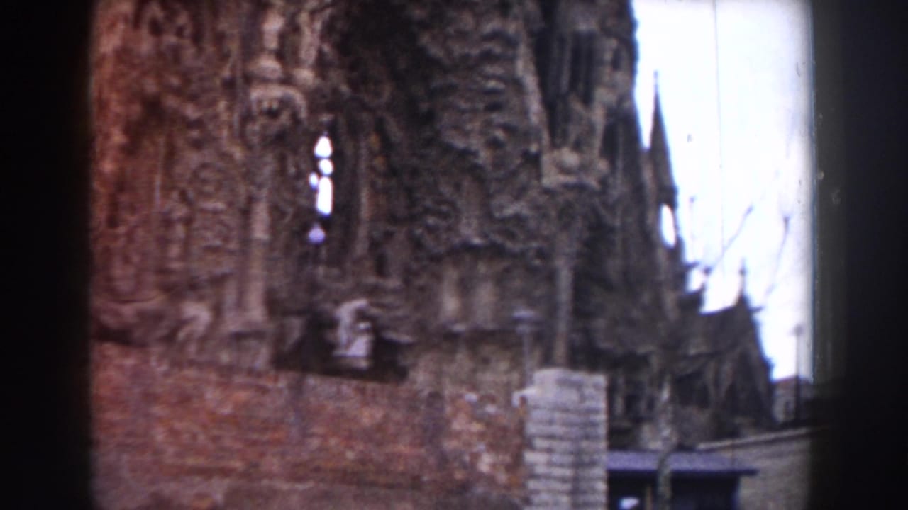 Church facade with carved stonework, brick wall, pale sky, and a distant spire.
