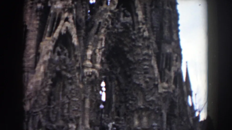 1959 Barcelona 8mm frame showing an ornate stone facade with pointed arches, sculptural carving, and bright sky behind the structure.