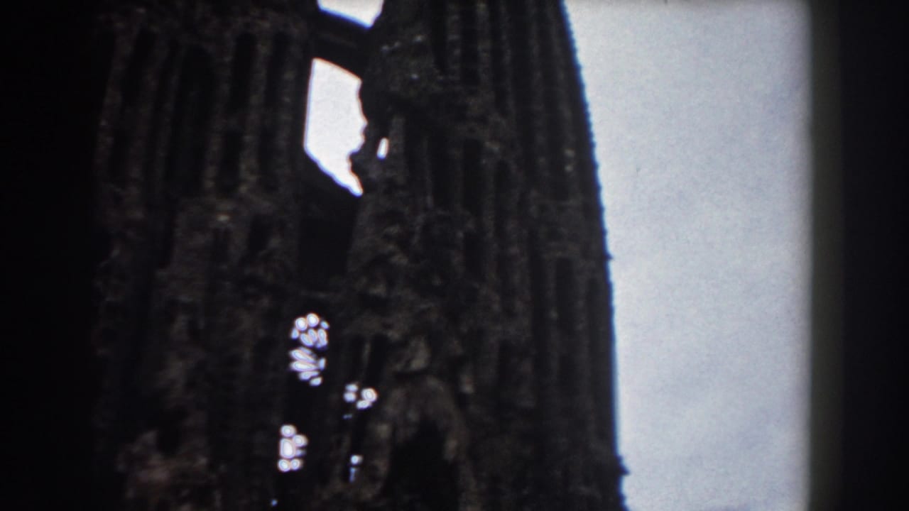 1959 Barcelona 8mm frame showing dark Gothic church or cathedral towers with damaged openings and pale sky behind them.