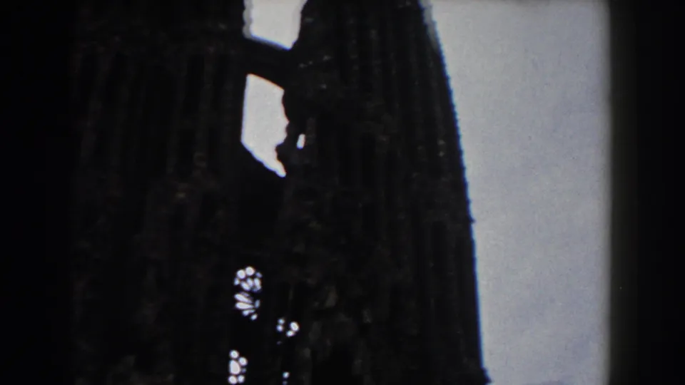 Close 1959 8mm view of a dark Barcelona church or cathedral tower, with rough stonework and pale sky along the frame edge.