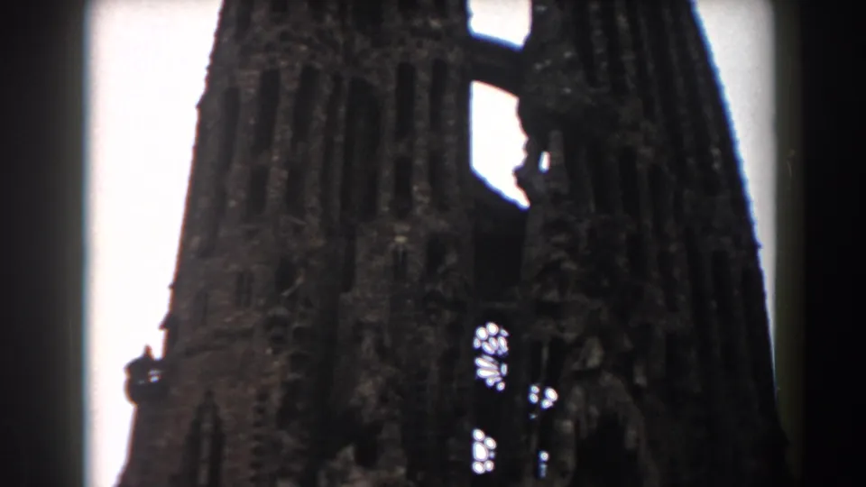 Barcelona 1959 8mm frame showing damaged stone church or cathedral towers, bright sky, and small openings in the facade.