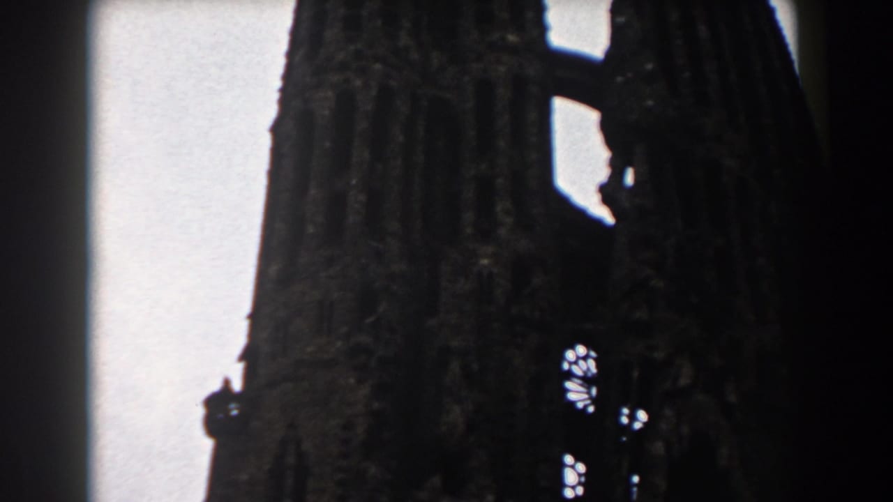 1959 Barcelona 8mm frame showing a dark Gothic church spire with small stained-glass openings against an overcast sky.