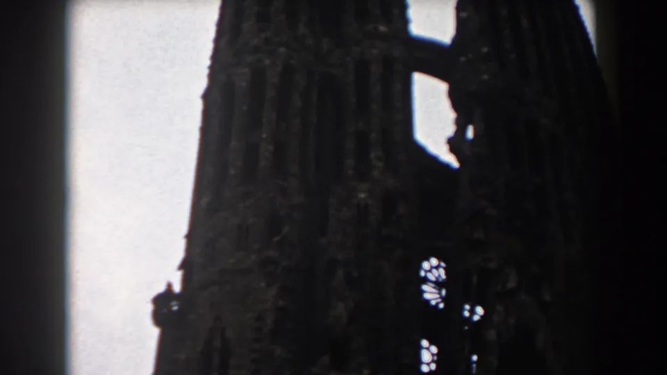 1959 Barcelona 8mm frame showing a dark Gothic church spire with small stained-glass openings against an overcast sky.