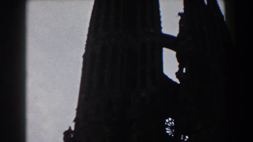 1959 Barcelona 8mm frame with a Gothic spire and adjacent dark architectural mass silhouetted in soft focus.