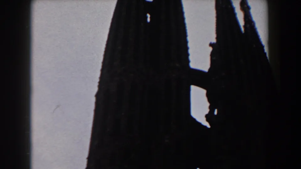 Low-angle 1959 Barcelona 8mm view of a tall Gothic church spire, heavily shadowed against the overcast sky.