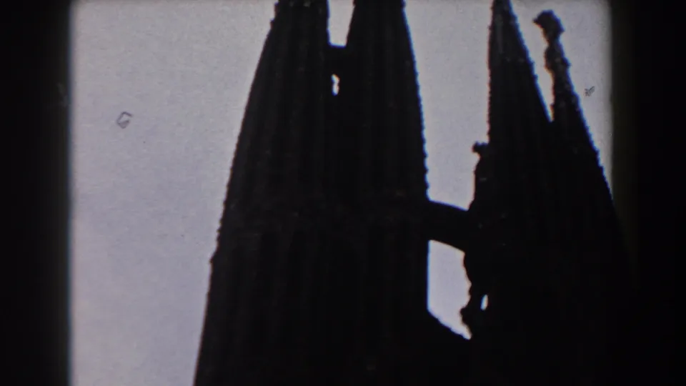 1959 Barcelona 8mm frame showing the upper portion of Gothic-style church spires in silhouette against a pale sky.