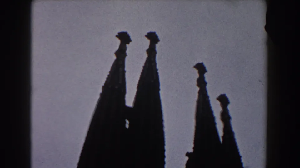 Silhouetted church towers in Barcelona, seen in soft 8mm focus with pale sky and dark frame border.
