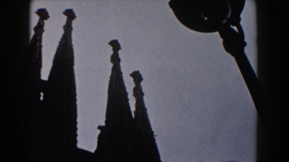1959 Barcelona 8mm frame with dark church spires and a street lamp silhouetted against a pale sky.