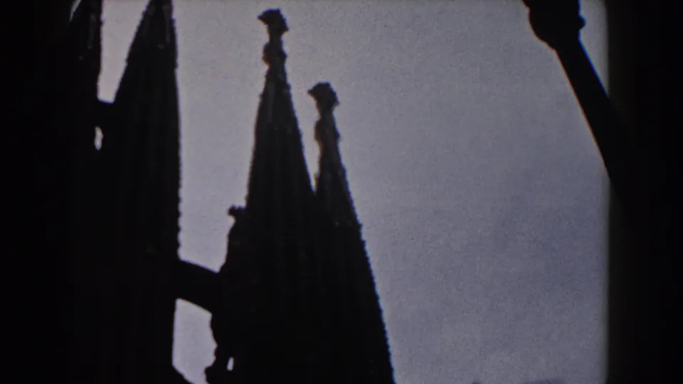 1959 Barcelona 8mm frame with cathedral spires partly obscured by a dark foreground structure and lamp.