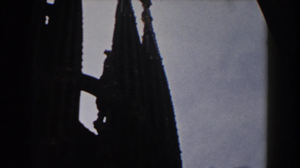 1959 Barcelona 8mm frame showing a tall Gothic spire in silhouette with adjacent dark stone forms.