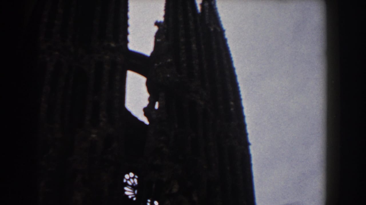 1959 Barcelona 8mm frame showing Sagrada Familia spires in dark silhouette against a pale sky.