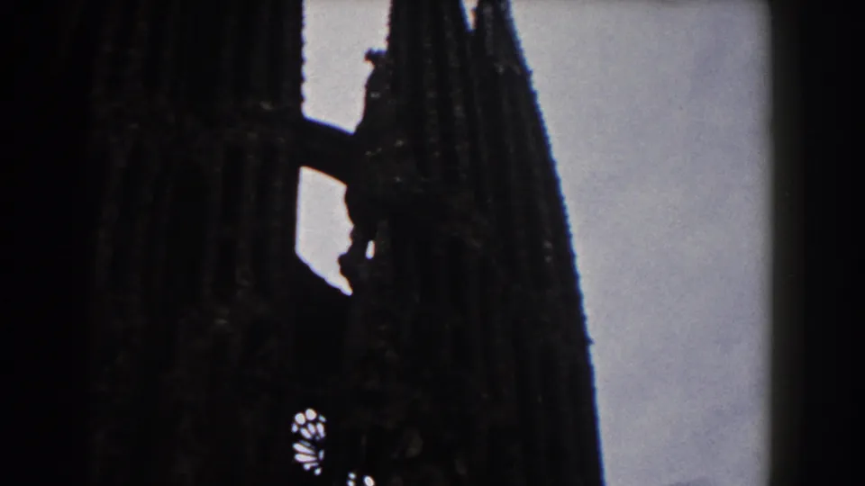 1959 Barcelona 8mm frame showing Sagrada Familia spires in dark silhouette against a pale sky.