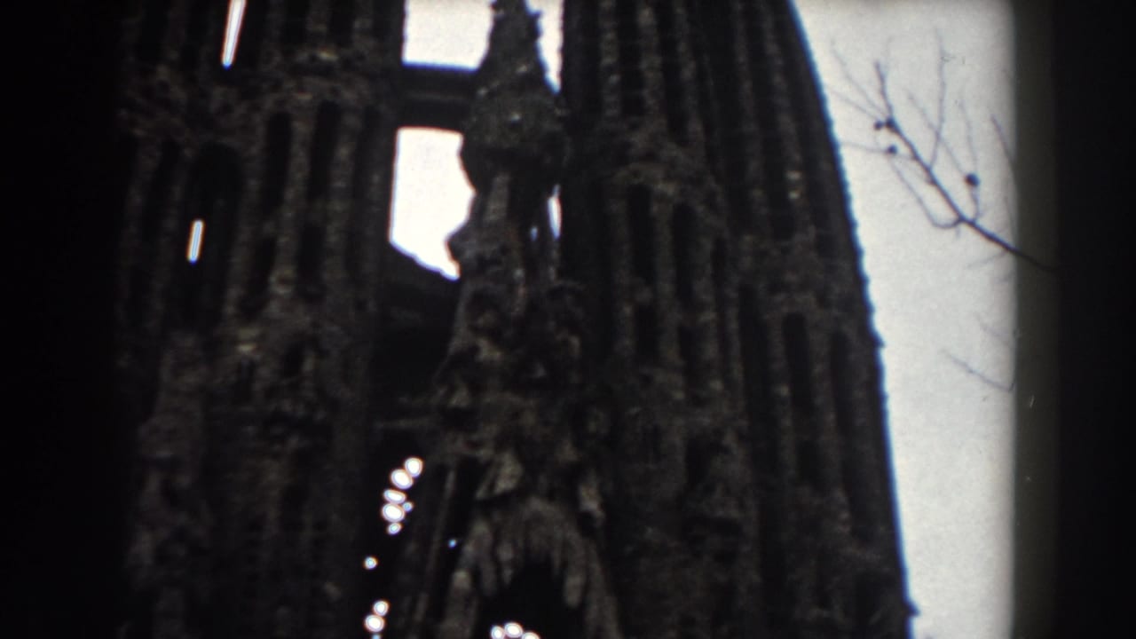 Low-angle view of a tall dark stone facade with arched openings and pale sky behind it.