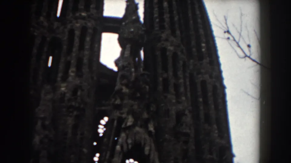 1959 Barcelona 8mm frame showing a low-angle view of a towering stone facade with narrow arches and carved vertical details.