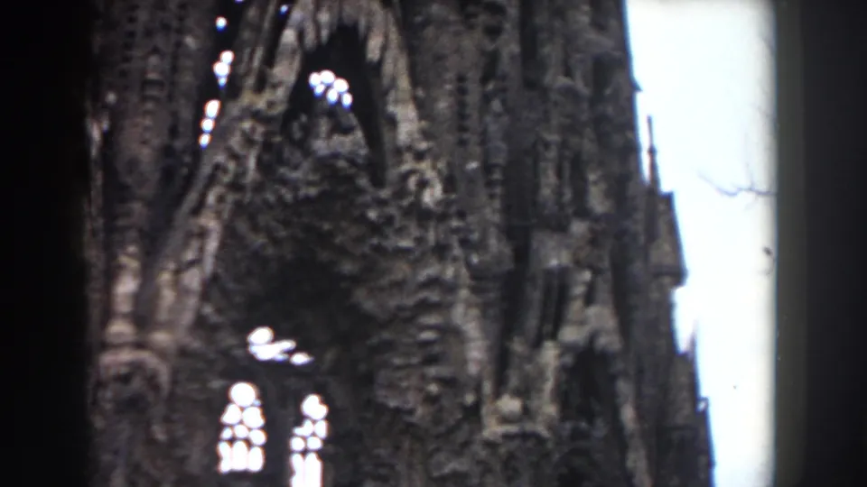 1959 Barcelona church detail showing dark Gothic-style stone carving, tracery, and bright arched windows in soft 8mm focus.