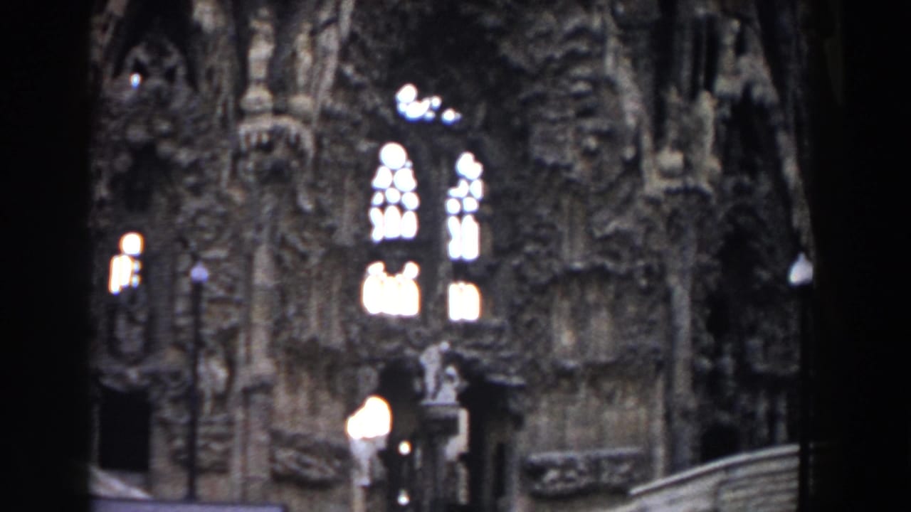 Ornate Sagrada Familia facade with arched windows, lamps, steps, and a visitor near the entrance.