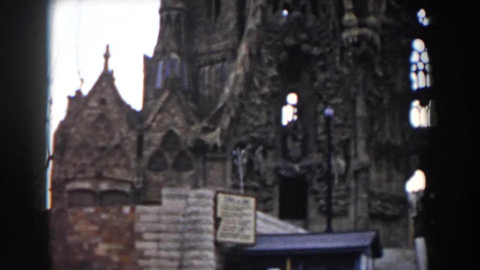 Barcelona church exterior in 1959, with dark arched openings, dense carved stonework, a foreground sign, fencing, and a lamppost.