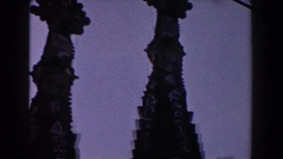 1959 Barcelona 8mm frame showing dark, ornate arched stone silhouettes rising against a pale sky.