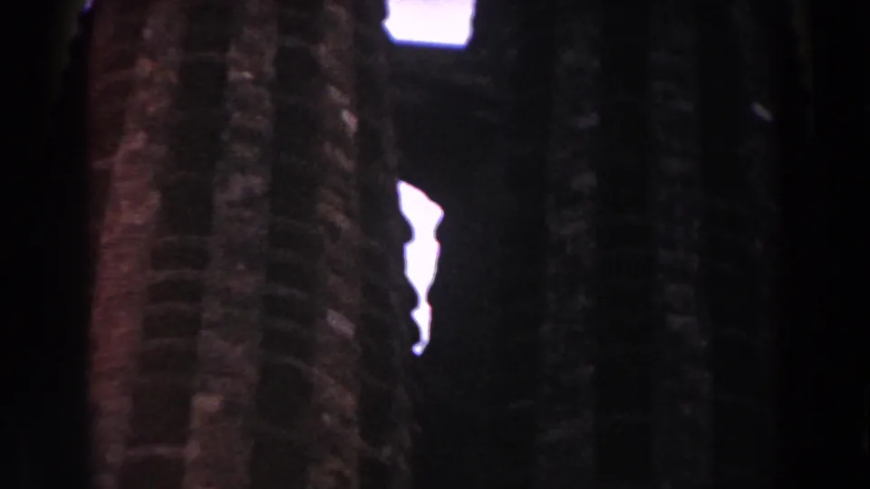 Close 8mm view of rough vertical masonry in Barcelona, with bright slits of sky between dark structural forms.