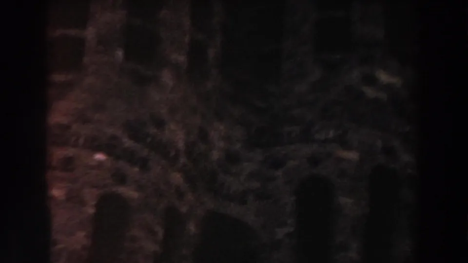 Shadowed 1959 Barcelona home-movie frame with rough stonework and a dark arch-like opening near the lower edge.
