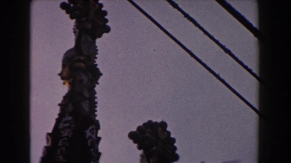 Barcelona cathedral spires remain in view as overhead utility wires cut diagonally across the pale sky in this 1959 8mm frame.