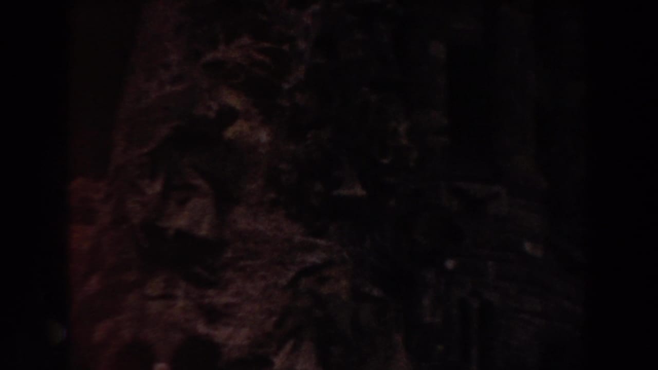 Dark, close view of rough carved stone inside a shadowed building.