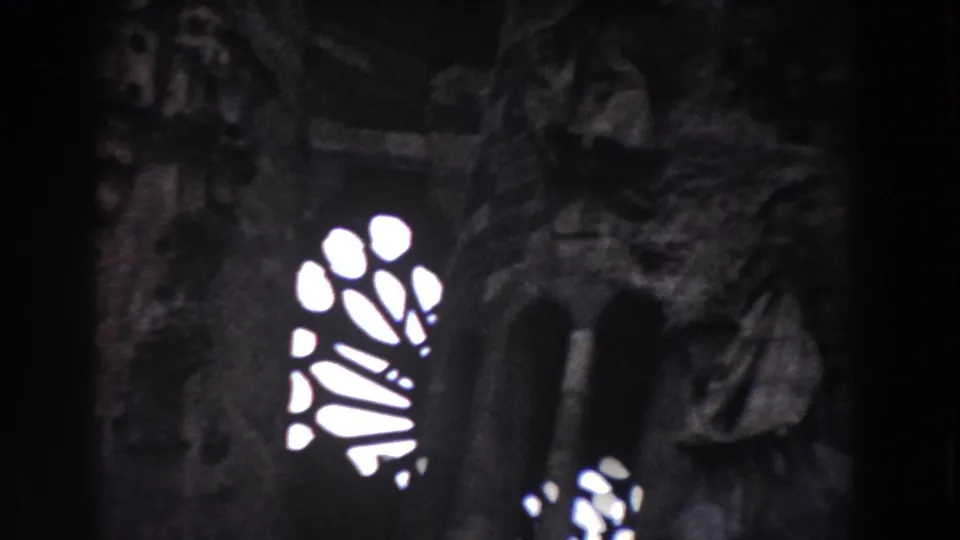 Dim Barcelona 8mm frame showing a bright stained-glass-like window pattern next to a shadowed stone figure and masonry.