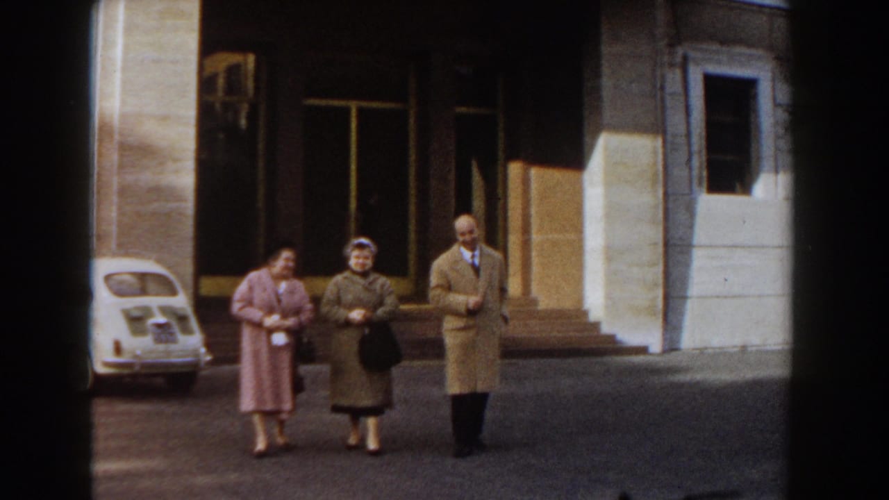 Two women and a man in coats continue walking past a parked white compact car.