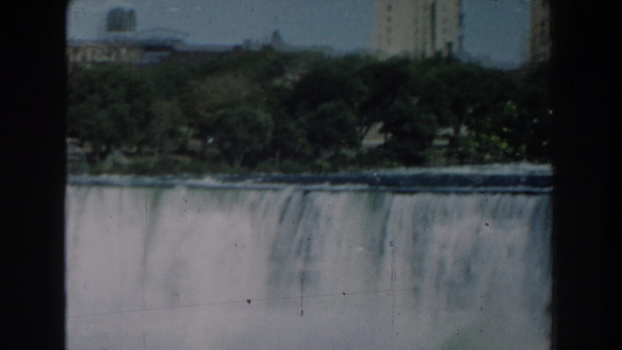A closer view of water cascading over the dam behind dark film-frame edges.