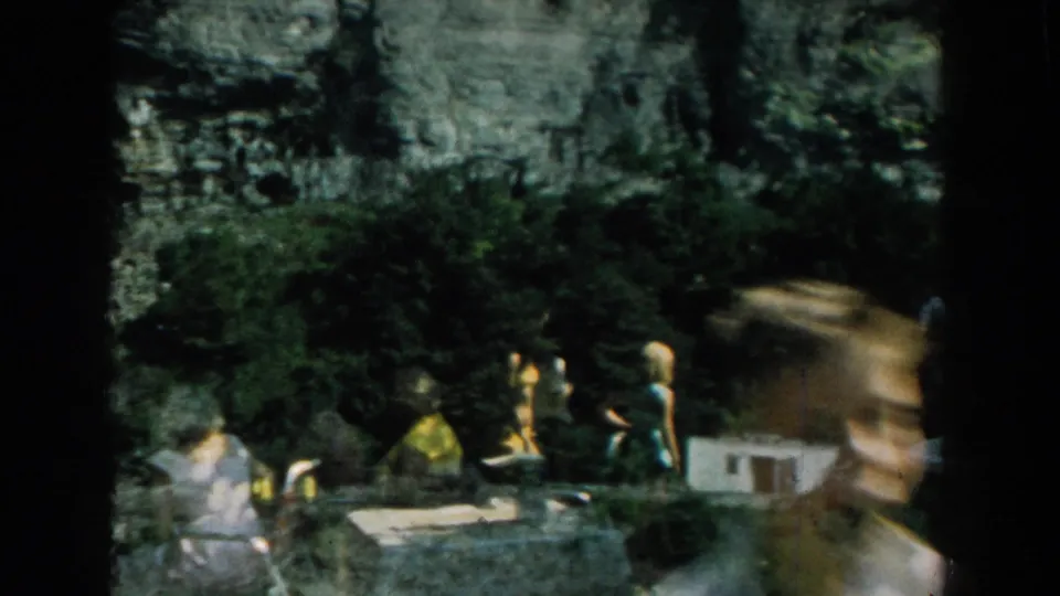 1959 Michigan home-movie frame showing a backyard with seated or standing figures, lawn chairs, trees, and strong 8mm frame shadows.
