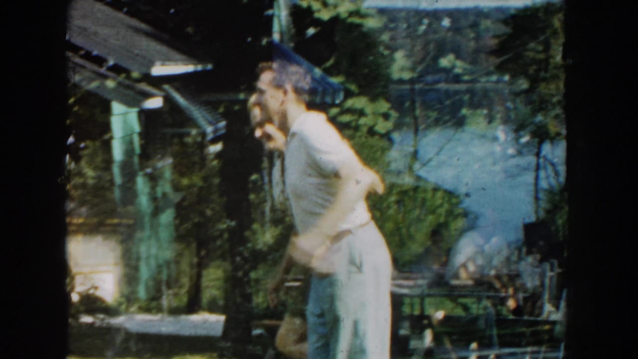 Man in light clothing dances with a woman near a cabin and lake.