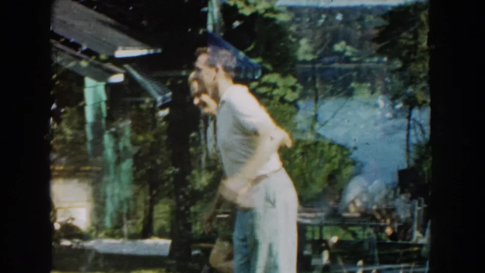 The dancing pair remains in the Michigan yard, with lake water, trees, and outdoor furniture visible behind the cabin area.